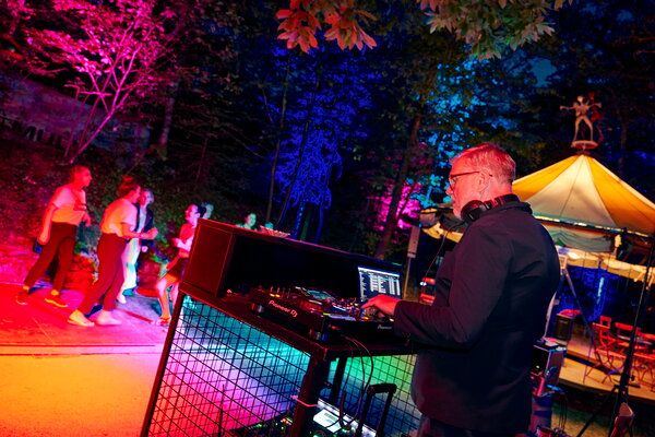 Seefest DJ legt bei einem beleuchteten Event auf, während im Hintergrund tanzende Menschen und ein Karussell zu sehen sind