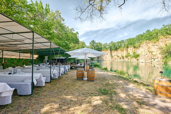 Seefest Festliches Outdoor-Event an einem Steinbruch mit See mit gedeckten Tischen, Sonnenschirmen und Weinfässern