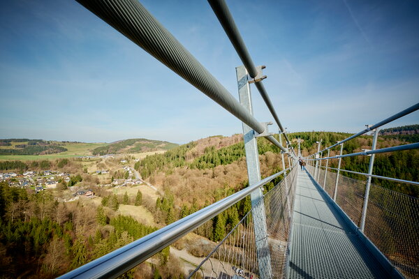 USU SPRING UP! in Willingen Blick über eine Hängebrücke mit Geländer und Stahlseilen auf eine bewaldete Landschaft