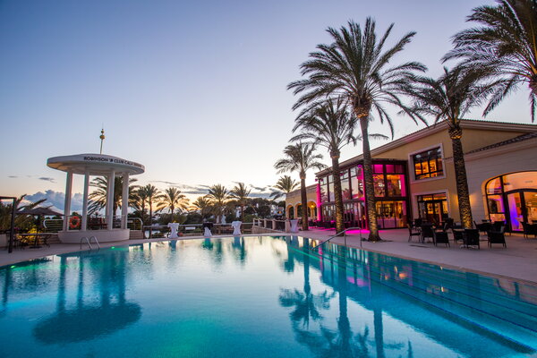Kick-off USU Mallorca, Luxuriöser Poolbereich mit Palmen und einem eleganten Gebäude bei Sonnenuntergang