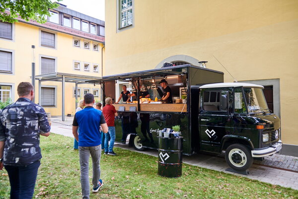 Kongress & Sommerfest Wolters Kluwer Scala Ein Foodtruck in einem grünen Innenhof mit mehreren Personen, die auf Essen warten