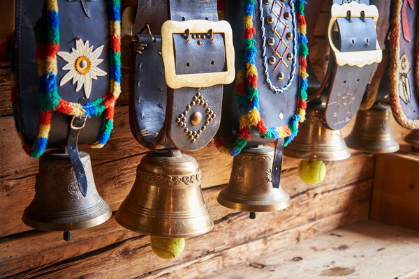 Incentive Sölden Traditionelle Almglocken mit bunten traditionellen Verzierungen und Alpenveilchen hängen vor einer Holzwand