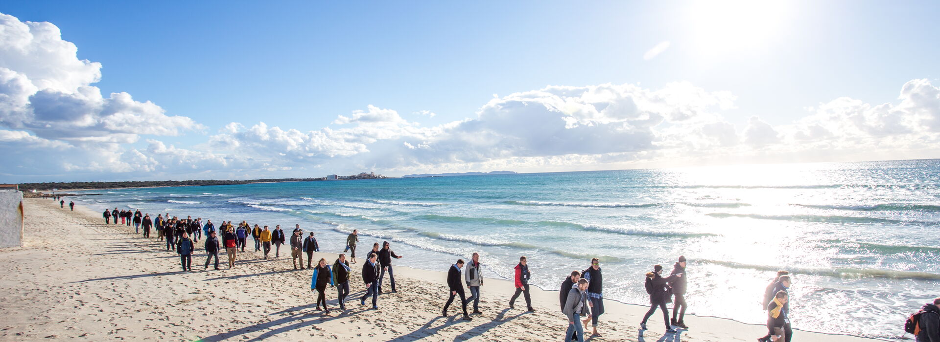 Kick-off USU Mallorca Menschenmenge macht einen Spaziergang am Strand mit Sonne und leichtem Wellengang am Nachmittag