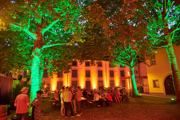 Kongress & Sommerfest Wolters Kluwer Scala eine lebhafte Nachtveranstaltung im Freien mit beleuchteten Bäumen und Menschen