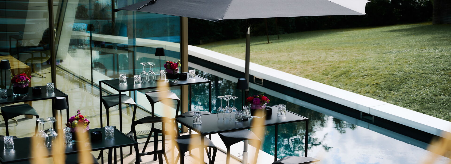 Müller Live-Kommunikation Außenbereich eines modernen Hauses mit Tischen, Sonnenschirm und Blick auf den Garten und Pool