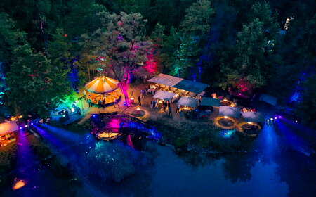 Seefest bei Nacht mit beleuchteten Ufer mit bunten Lichtern, Karussell und einer festlichen Atmosphäre inmitten von Bäumen