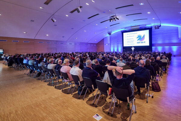 USU SPRING UP! in Willingen Vortragender spricht vor großem Publikum in einem Konferenzsaal mit "JUST DO IT" auf der Leinwand
