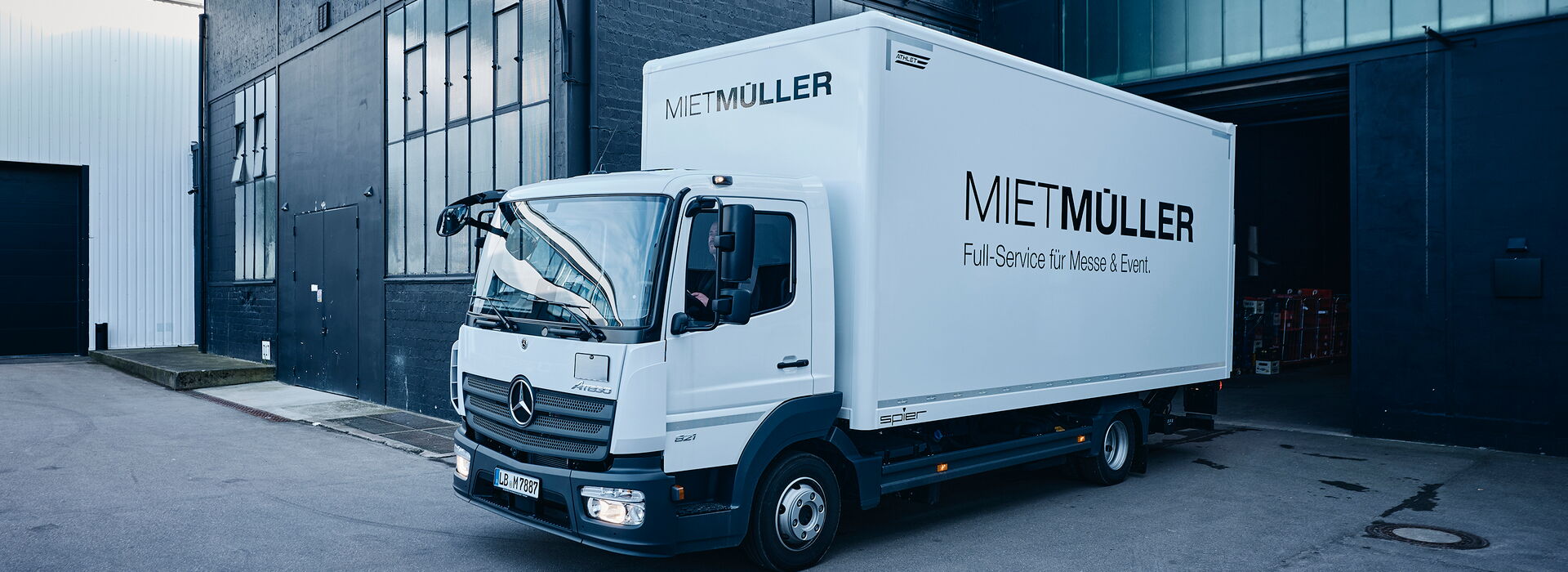 Der MIETMÜLLER Transporter steht vor einem modernen Lagergebäude, bereit für den Transport von Messe- und Eventmaterial