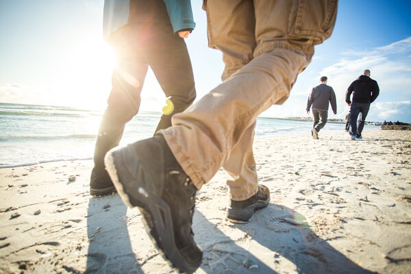 Kick-off USU Mallorca, Gruppe von Menschen, die am Strand entlang spazieren, die Sonne im Hintergrund scheint und Wellen