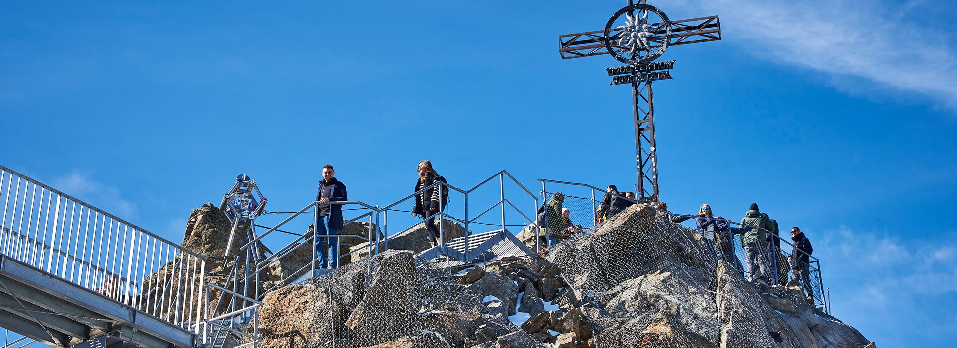 Incentive Sölden die Besucher stehen auf einem Berggipfel mit einem großen Kreuz, umgeben von Felsen und Schnee