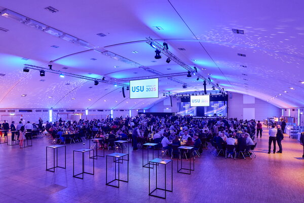 USU SPRING UP! in Willingen Großer Saal mit vielen sitzenden Gästen, Bühne mit "USU NIGHT 2025"-Logo und blauer Beleuchtung