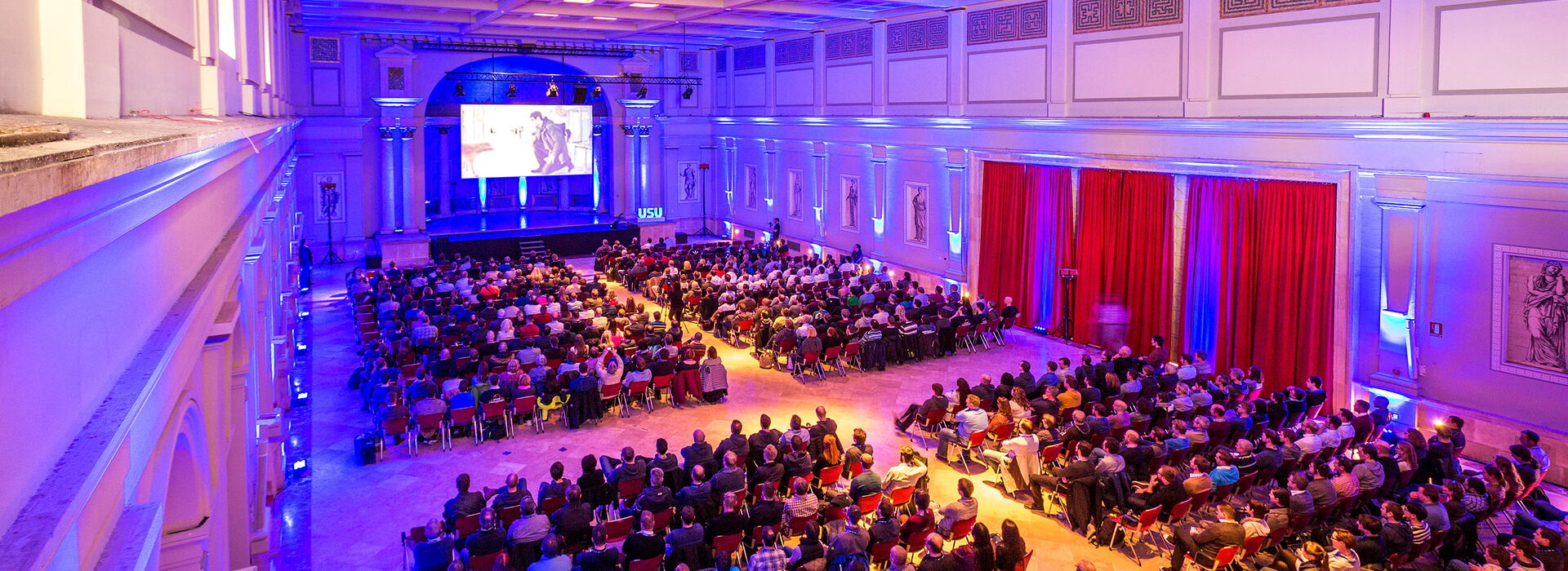 Kick-off USU Mallorca eine große Menschenmenge sitzt in einem beleuchteten Saal während einer Veranstaltung mit Präsentation