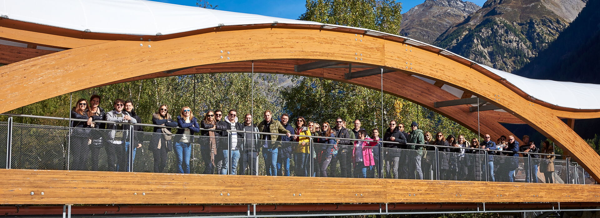 Incentive Sölden Gruppe von Menschen auf einer modernen Holzbrücke mit Bergpanorama und Fluss