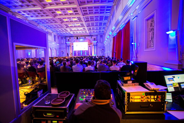 Kick-off USU Mallorca mit Blick auf eine Menschenmenge bei einer Konferenz, mit einem Redner auf der Bühne und Mischpult