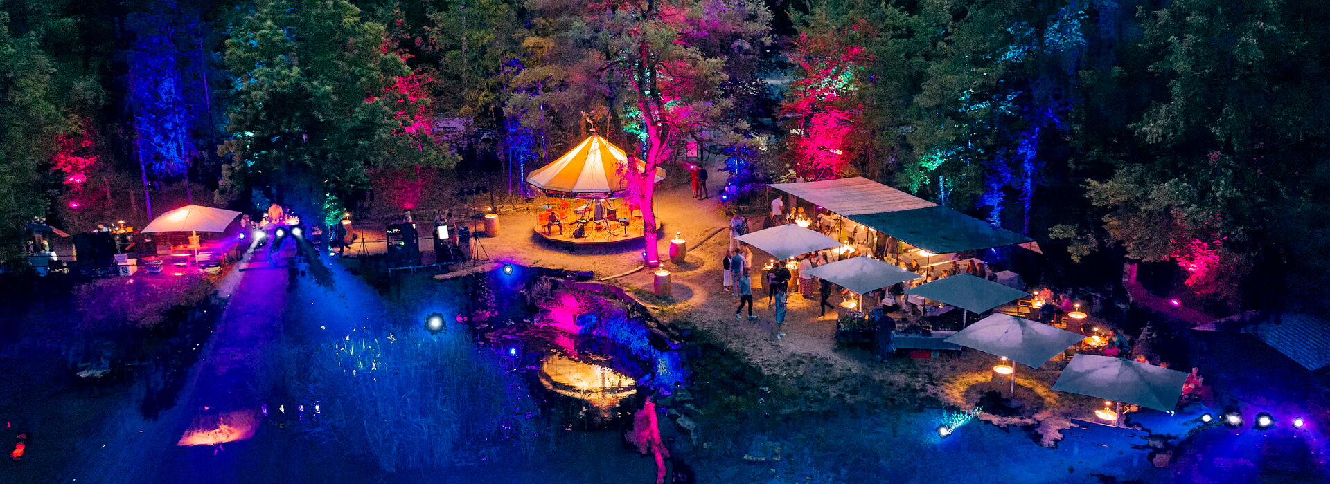 Seefest bei Nacht mit beleuchteten Ufer mit bunten Lichtern, Zelten und einer festlichen Atmosphäre inmitten von Bäumen