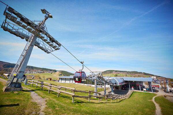 USU SPRING UP! in Willingen Rote Gondel einer Seilbahn fährt bergauf mit Berglandschaft und Station im Hintergrund